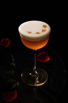Cocktail ambré avec mousse blanche et pétales de rose.