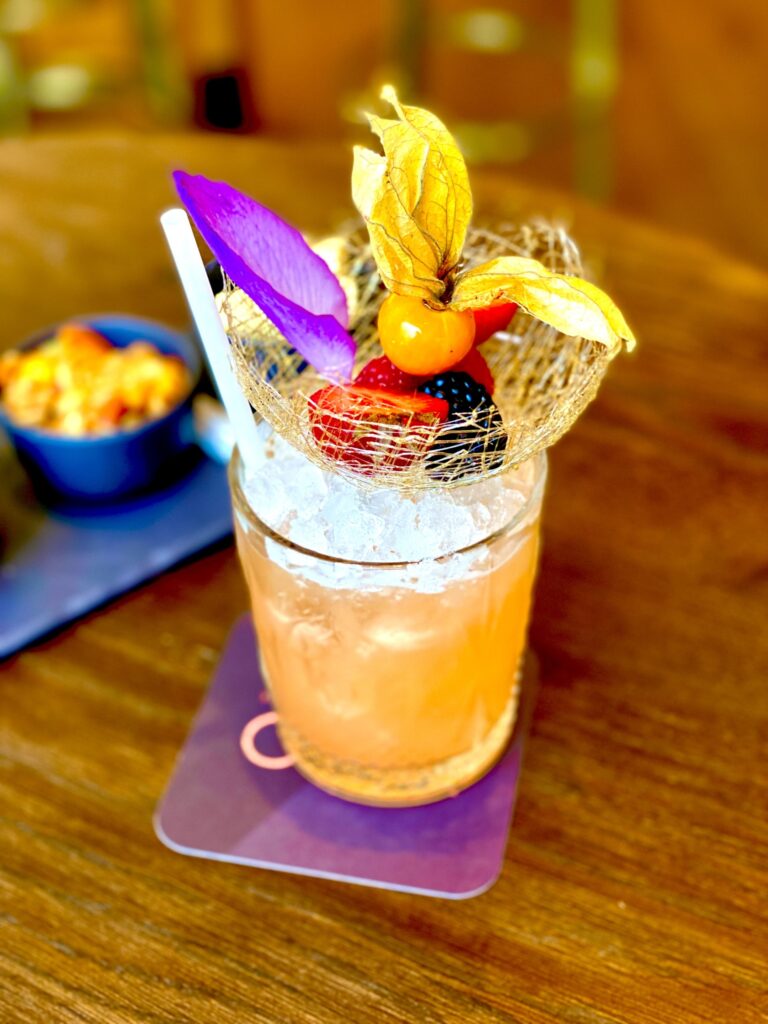 Cocktail premium orange garni de fruits rouges, physalis et pétale violet dans nid doré