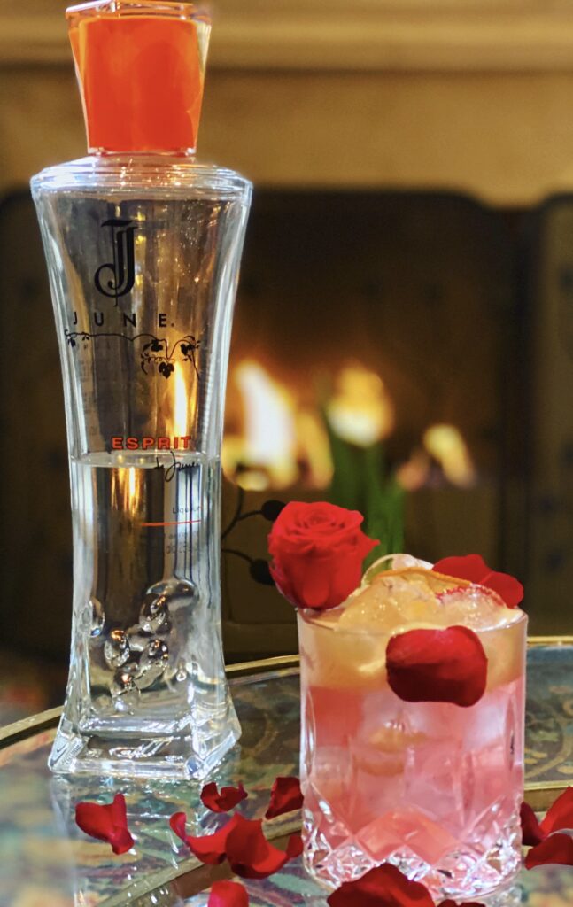 Bouteille JUNE Esprit et cocktail rose aux pétales de rose devant cheminée élégante