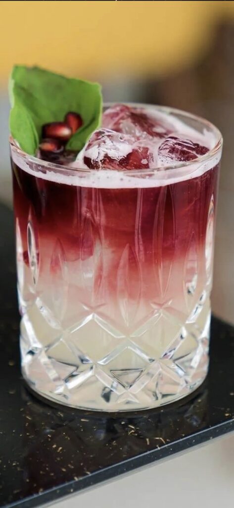 Cocktail premium dégradé blanc et rouge avec glaçons, feuille verte et graines de grenade