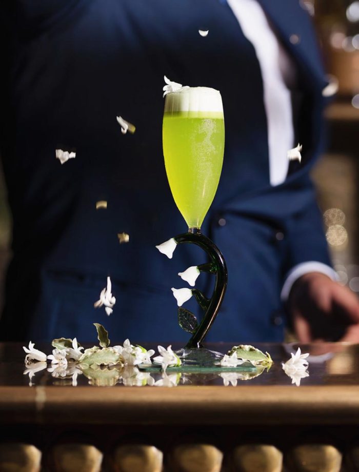 Cocktail signature vert présenté sur un support décoratif – Nomad Bar